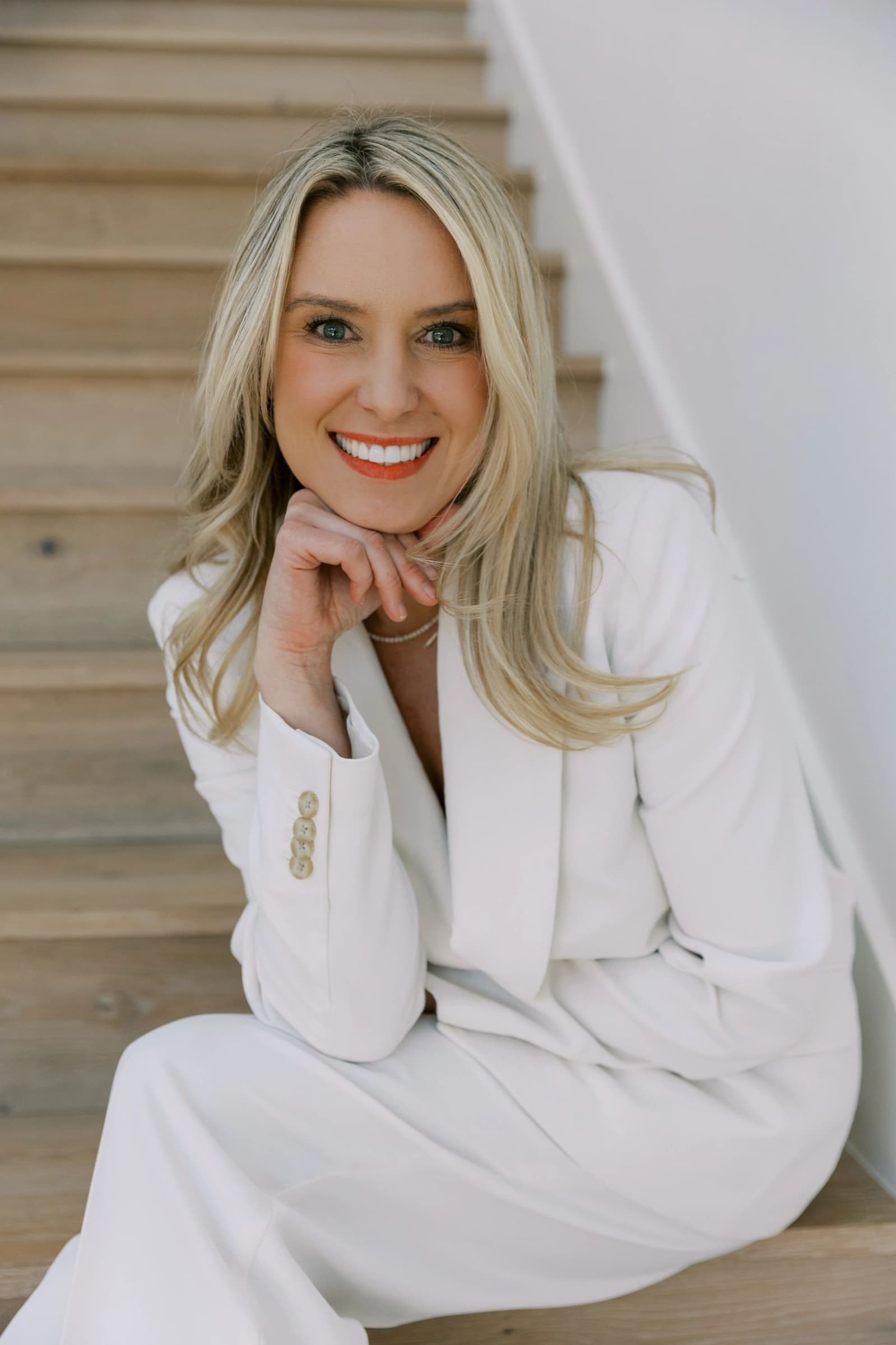 Brittany Moore in a white suit, smiling, seated on an oak staircase